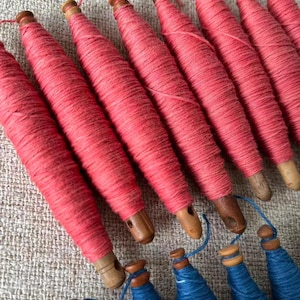 May include: Close-up of several pink thread spools with wooden bases, arranged diagonally. Below, a few blue thread spools are visible. The spools are likely for sewing or crafting, showcasing a variety of colors and textures.