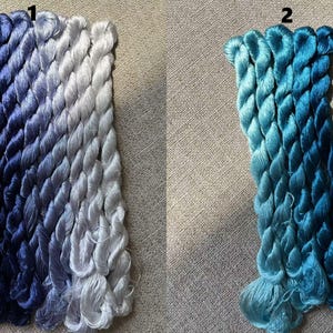 Pode incluir: Dois conjuntos de fio para bordar, um em tons de azul e cinza, e o outro em tons de azul. O fio est&aacute; organizado em feixes e etiquetado com os n&uacute;meros 1 e 2.