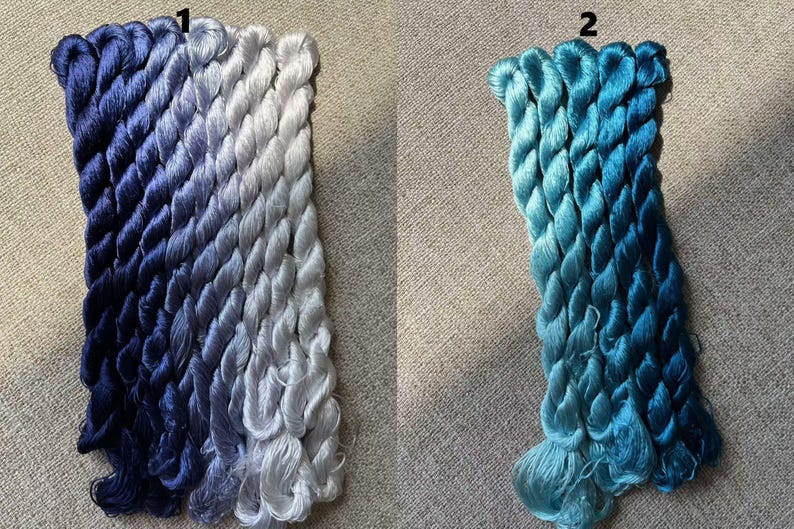 Pode incluir: Dois conjuntos de fio para bordar, um em tons de azul e cinza, e o outro em tons de azul. O fio est&aacute; organizado em feixes e etiquetado com os n&uacute;meros 1 e 2.