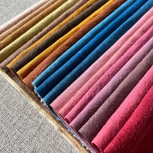 Könnte beinhalten: Eine Sammlung von Stoffmustern in verschiedenen Farben, darunter Brauntöne, Gelb, Blau, Rosa und Rot. Die Muster sind diagonal angeordnet und zeigen die unterschiedlichen Texturen und Farbtöne des Stoffes.