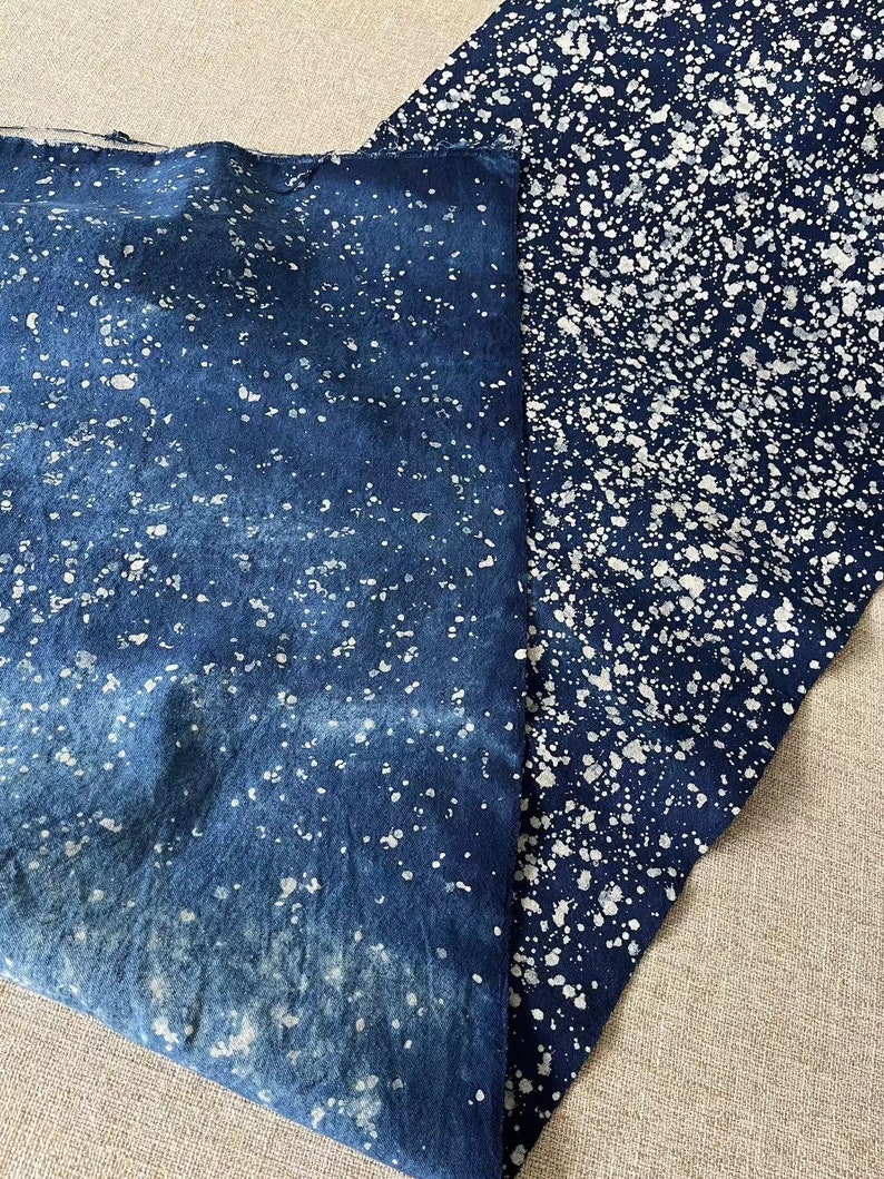 May include: Two pieces of blue fabric with a white splatter pattern. The fabric is folded and the white splatter pattern is more dense on one piece of fabric than the other.