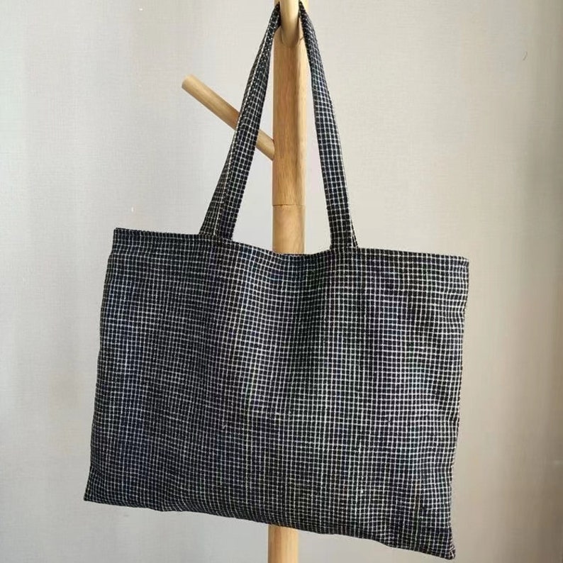 May include: A black and white checkered tote bag with fabric handles. The bag is hanging on a wooden stand.