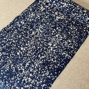 May include: A roll of dark blue fabric with a white splatter pattern. The fabric is rolled up and the end is visible.