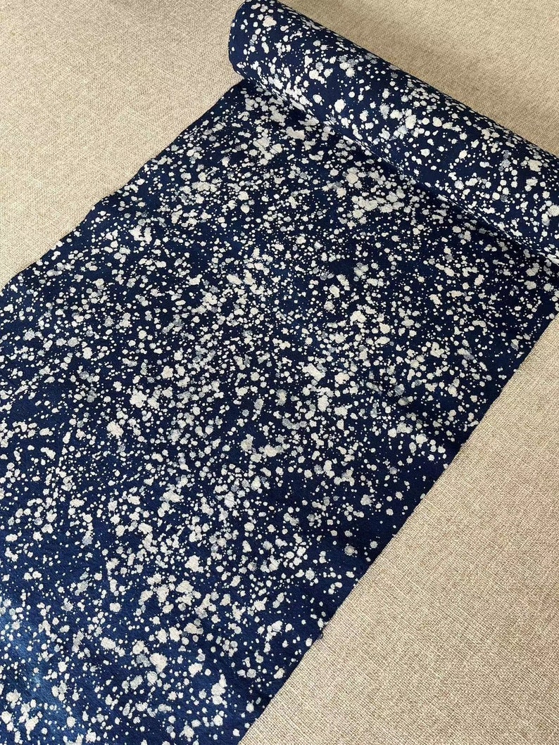 May include: A roll of dark blue fabric with a white splatter pattern. The fabric is rolled up and the end is visible.