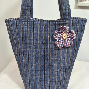 May include: A blue and white striped tote bag with a red and white checkered flower accent. The bag has two handles and a wide opening.