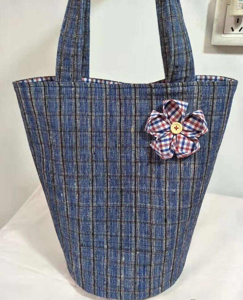 May include: A blue and white striped tote bag with a red and white checkered flower accent. The bag has two handles and a wide opening.