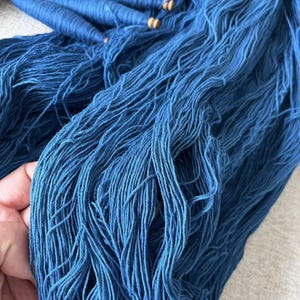 K&ouml;nnte beinhalten: Ein Stapel tiefblauer Garnrollen mit Holzspulen und losen Garnstr&auml;ngen.