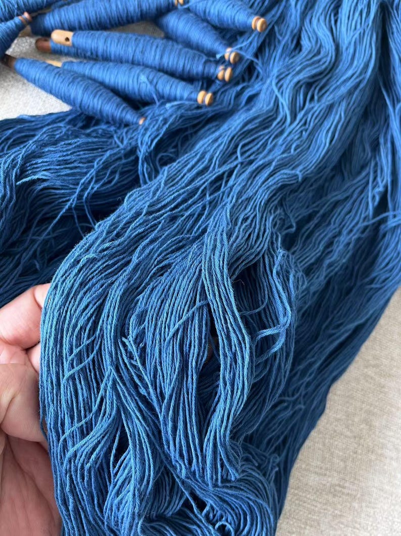 K&ouml;nnte beinhalten: Ein Stapel tiefblauer Garnrollen mit Holzspulen und losen Garnstr&auml;ngen.
