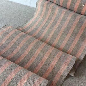 Può includere: Primo piano di un tessuto con un motivo a righe. Il tessuto presenta strisce alternate grigie e corallo. Il tessuto è ripiegato su se stesso, creando un effetto a strati. Il tessuto sembra essere lino o un materiale simile tessuto.