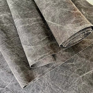 May include: Two rolls of dark gray fabric with a textured, crinkled surface. The fabric is folded and rolled up.