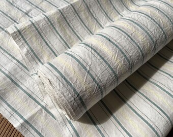 May include: A roll of white fabric with thin, green stripes. The fabric has a textured, slightly wrinkled appearance.