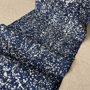 May include: A close-up of a dark blue fabric with a white splatter pattern. The fabric is folded and has a soft, textured appearance.