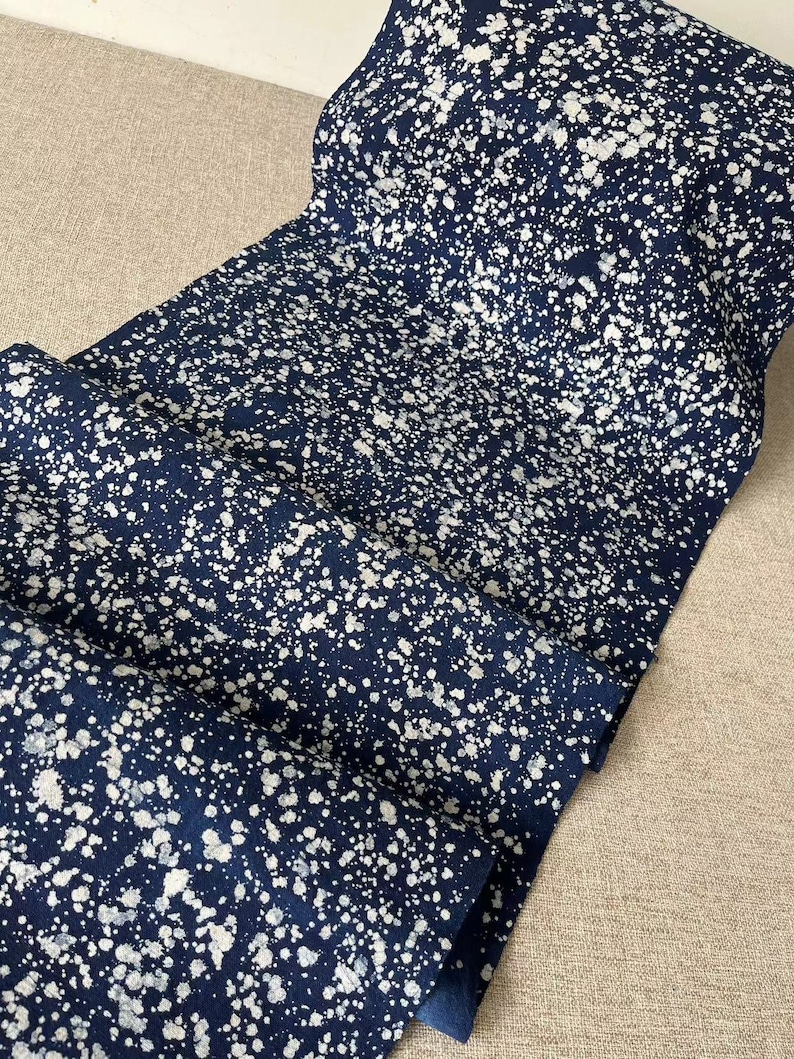 May include: A close-up of a dark blue fabric with a white splatter pattern. The fabric is folded and has a soft, textured appearance.