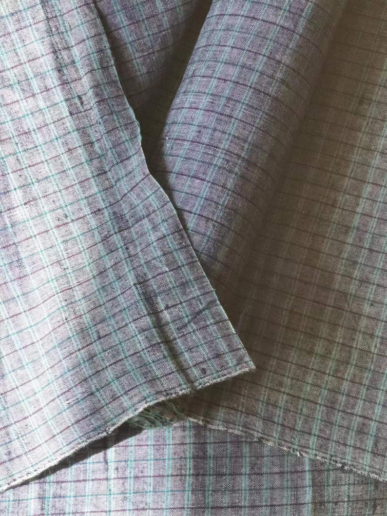 May include: Two pieces of fabric folded together, both are a light blue and dark gray plaid pattern.