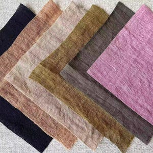May include: A selection of fabric samples in shades of navy, peach, beige, olive green, and mauve. The textiles have a textured finish, possibly linen or a similar woven material. The samples are arranged diagonally, showcasing the different colours.