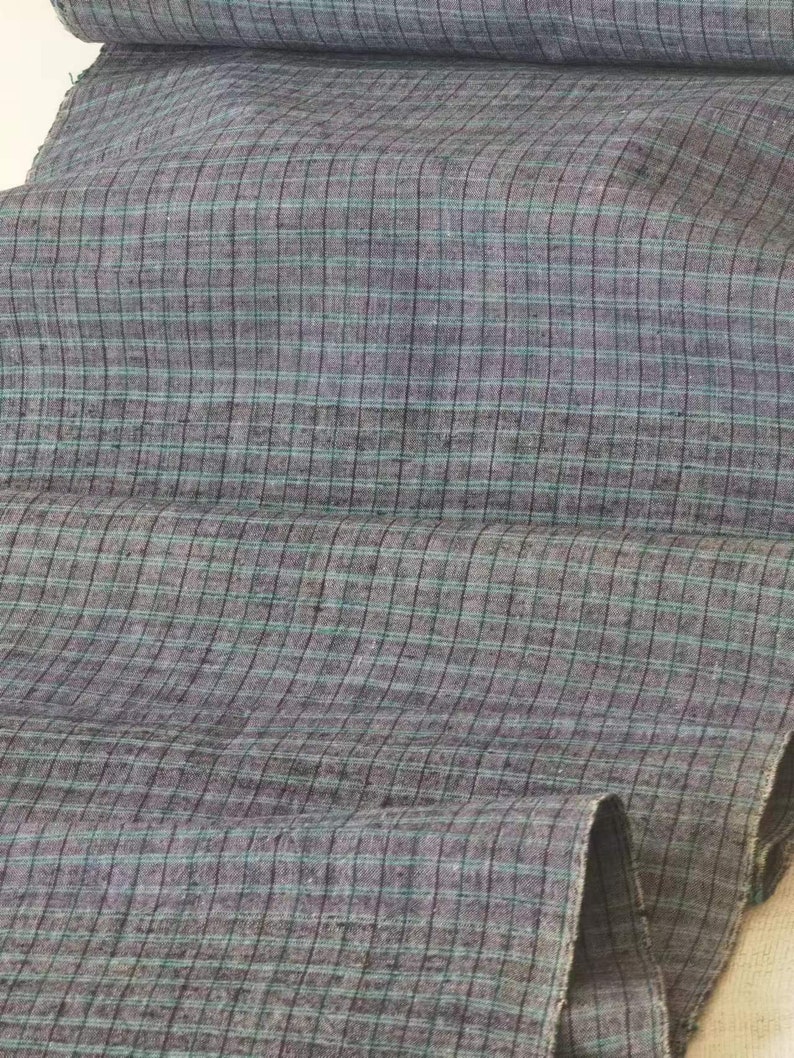 May include: A close-up of a gray and blue checkered fabric. The fabric has a subtle sheen and a soft texture.