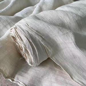 May include: A roll of off-white linen fabric, partially unrolled, displaying the texture and weave of the material. The fabric has a natural, slightly wrinkled appearance, suggesting a soft and breathable textile. The neutral color makes it suitable for various uses.
