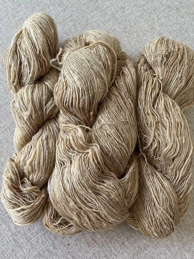 May include: A skein of natural colored yarn with a subtle fleck of brown. The yarn is made of a soft, natural fiber and is perfect for knitting or crocheting.