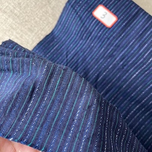 May include: A close-up of a blue and green striped fabric with silver thread woven in. The fabric is 58 inches wide. The number "3" is written on a red label.