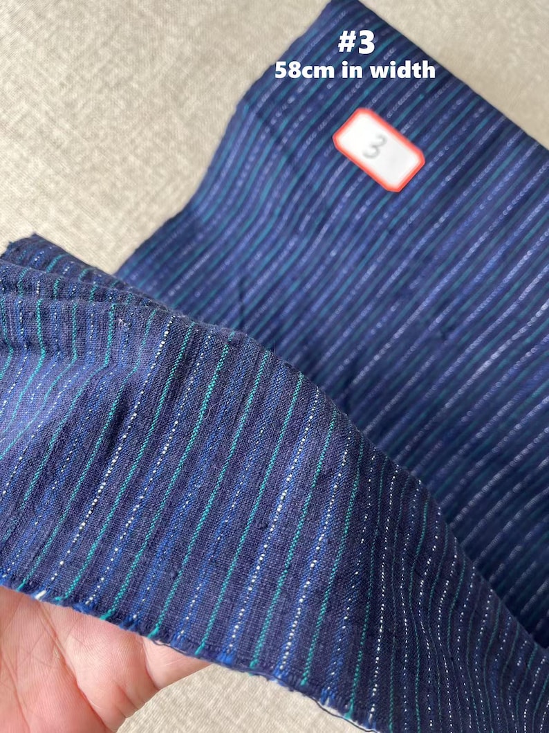 May include: A close-up of a blue and green striped fabric with silver thread woven in. The fabric is 58 inches wide. The number "3" is written on a red label.
