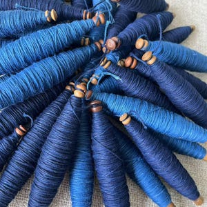K&ouml;nnte beinhalten: Eine Sammlung blauer Garnrollen mit Holzenden. Das Garn ist fest gewickelt und hat einen Farbverlauf in Blaut&ouml;nen.