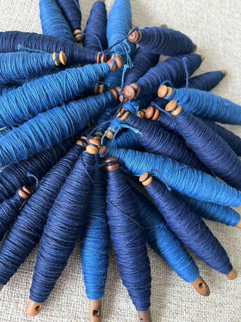 K&ouml;nnte beinhalten: Eine Sammlung blauer Garnrollen mit Holzenden. Das Garn ist fest gewickelt und hat einen Farbverlauf in Blaut&ouml;nen.