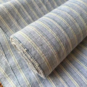 May include: A roll of blue and white striped fabric. The fabric is a light blue with vertical stripes of white and a hint of green. The fabric is rolled up, with some of it unrolled and lying flat.