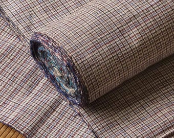 May include: A roll of brown and white plaid fabric with a blue and red trim. The fabric is woven with a fine checkered pattern.