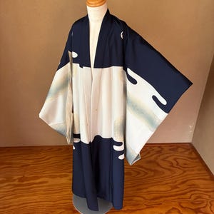 以下が含まれることがあります： 波模様の紺と白の着物。マネキンに着せられており、その流れるようなデザインが際立っています。袖と下部は紺色で、中央とアクセントは白色です。