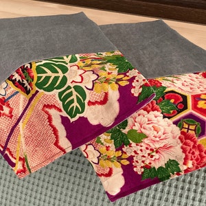 May include: Two gray linen pillow covers with colorful floral patterns. The patterns feature a mix of pink, red, yellow, green, and purple flowers and geometric shapes.