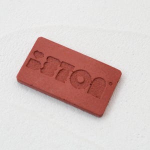 Pode incluir: Um rótulo retangular vermelho com a palavra "Stron" em relevo em branco.