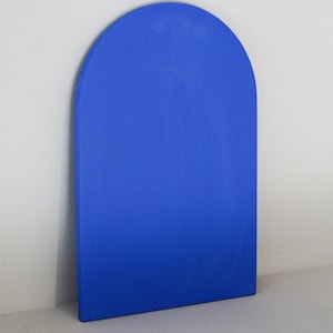 Può includere: Pannello decorativo blu pieno, a forma di arco. Il pannello è di una tonalità blu vibrante e ha una finitura liscia e opaca. La forma è un rettangolo alto con la parte superiore arrotondata, appoggiato a un muro bianco.