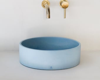 May include: A light blue round concrete vessel sink with a brass faucet and a brass handle.