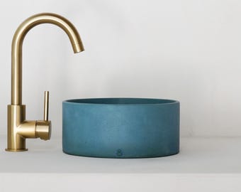 May include: A blue concrete vessel sink with a gold faucet. The sink is round and has a smooth, textured surface.