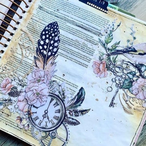 以下が含まれることがあります： 鳥、羽根、花、時計が描かれたヴィンテージスタイルのジャーナルページ。ページは、鍵、羽根、時計など、さまざまなエフェメラで飾られています。ページは、バラやその他の開花植物など、さまざまな花で飾られています。ページは、ミクストメディアアートの美しい例です。