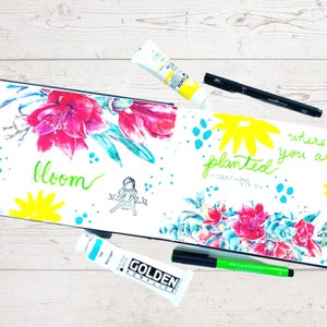 May include: An open sketchbook with a watercolor painting of flowers and the words "bloom" and "where you are planted" written in green marker. The page also includes a small drawing of a person and a quote from 1 Corinthians 9:19-24.