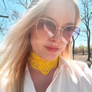 Puede incluir: Una mujer con una camisa blanca y un collar de encaje amarillo. Lleva gafas de sol de ojo de gato con un tinte rosado.