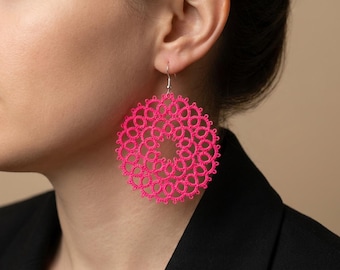 Puede incluir: Pendientes circulares de color rosa brillante con un diseño calado delicado. Los pendientes cuelgan de ganchos plateados. Un accesorio vibrante y audaz. Los pendientes son una pieza llamativa.