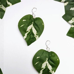 May include: A pair of earrings featuring green and white leaves with silver hooks.