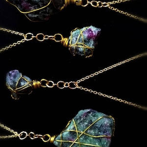May include: Four gold necklaces with green and pink gemstone pendants wrapped in gold wire. The gemstones are irregular in shape and have a rough, natural texture.