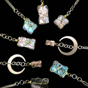 May include: A collection of eight necklaces featuring iridescent abalone shell pendants wrapped in brass wire. The pendants are rectangular and display a range of colours and patterns. Some of the necklaces include a crescent moon charm.
