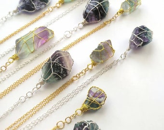 May include: A collection of nine necklaces featuring wire-wrapped fluorite crystals in shades of green, purple, and white. Each crystal is unique in shape and size, and the necklaces are strung on silver and gold chains.