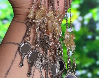May include: A collection of silver necklaces with small, ornate mirrors and clear, yellow-toned gemstone beads.