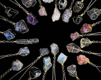 May include: A collection of 20 unique crystal necklaces with gold chains. Each necklace features a different type of crystal, including amethyst, rose quartz, and clear quartz. The crystals are wrapped in gold wire and hang from delicate gold chains.