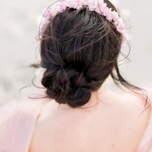 May include: A woman with dark brown hair styled in a messy bun, wearing a pink flower crown.