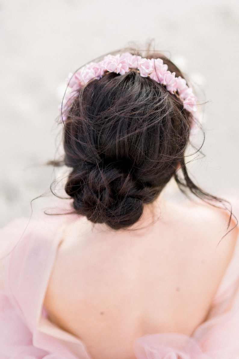 May include: A woman with dark brown hair styled in a messy bun, wearing a pink flower crown.