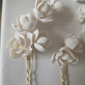May include: Set of three white ceramic flower hair pins with gold bobby pins. The flowers are delicate and have a realistic look.