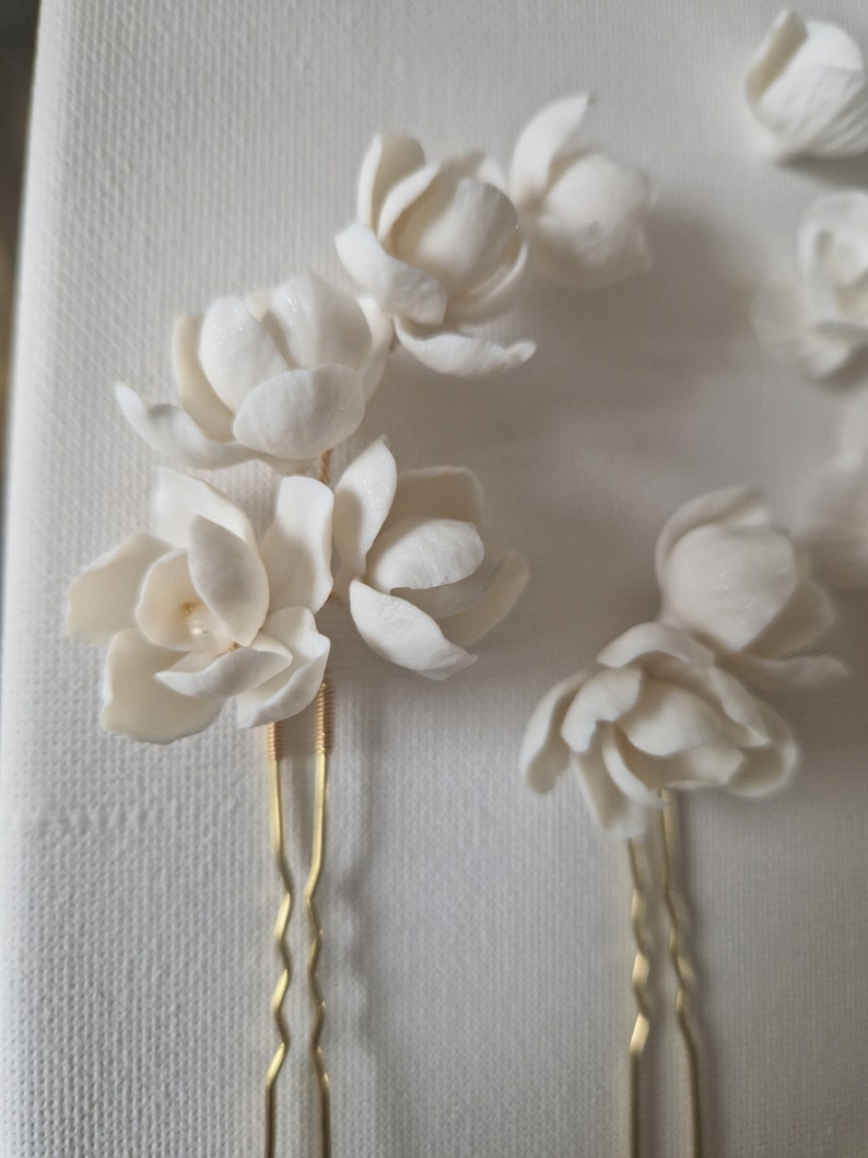 May include: Set of three white ceramic flower hair pins with gold bobby pins. The flowers are delicate and have a realistic look.