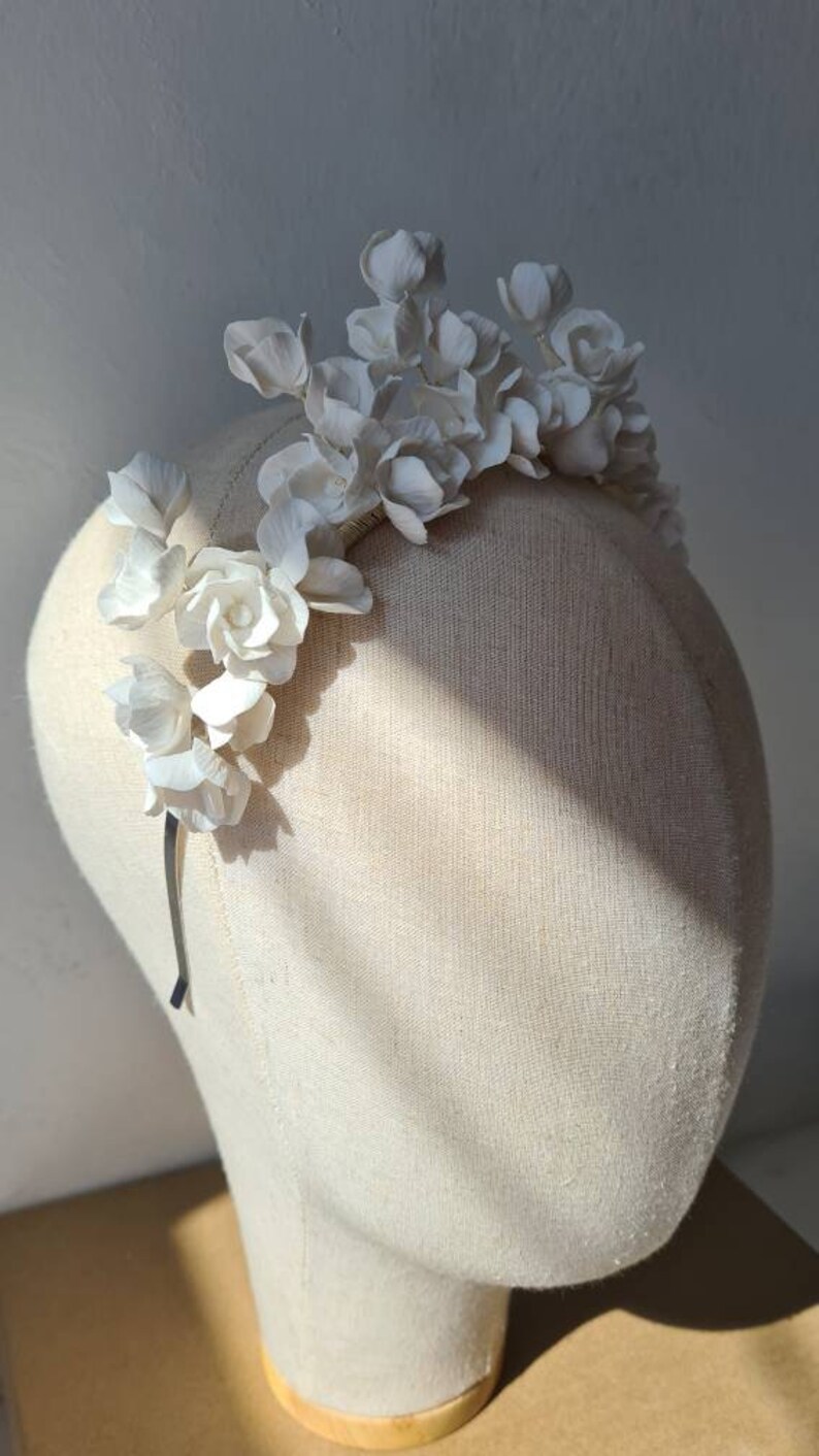 May include: A white floral headband with delicate white flowers arranged in a cascading design. The headband is made of a thin wire and is designed to be worn on the head.