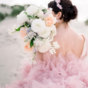 May include: A bride wearing a pink tulle dress with a large bouquet of white and peach flowers. The bouquet is held in front of her, obscuring her face.